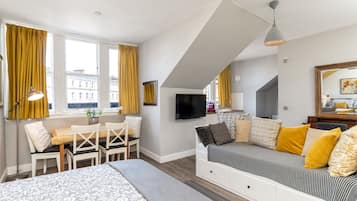 Ein modernes Schlafzimmer mit einem Bett, einer Couch, einem Fernseher und einem Essbereich mit Tisch und Stühlen.