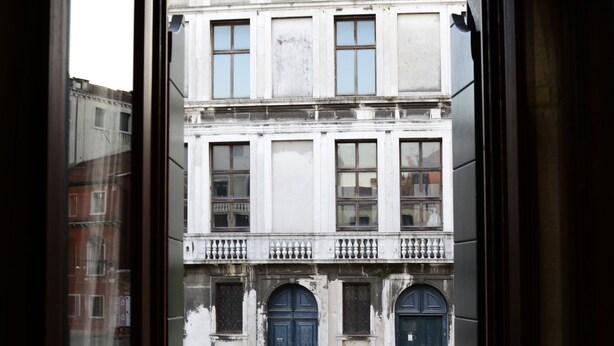 A view through a window of a building with multiple stories, a balcony, and a canal in the foreground. - Hotel Leone (Venice)