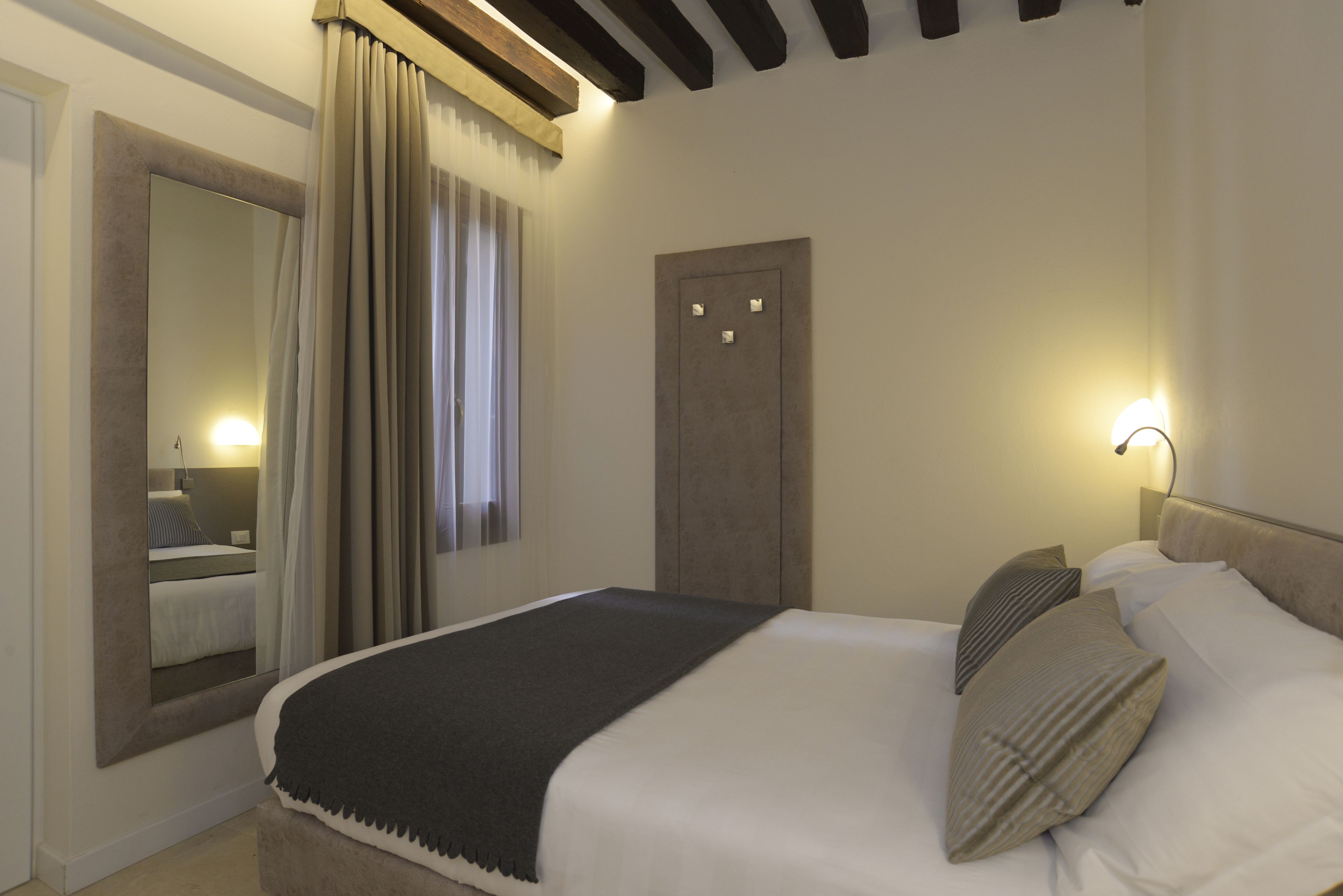 A bedroom with a large bed, a mirror, a door, and a nightstand with a lamp.