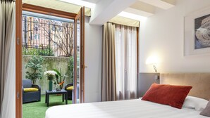 A hotel room with a bed, a view of the outside, a small table with a vase, and a chair. - Hotel Leone (Venice)