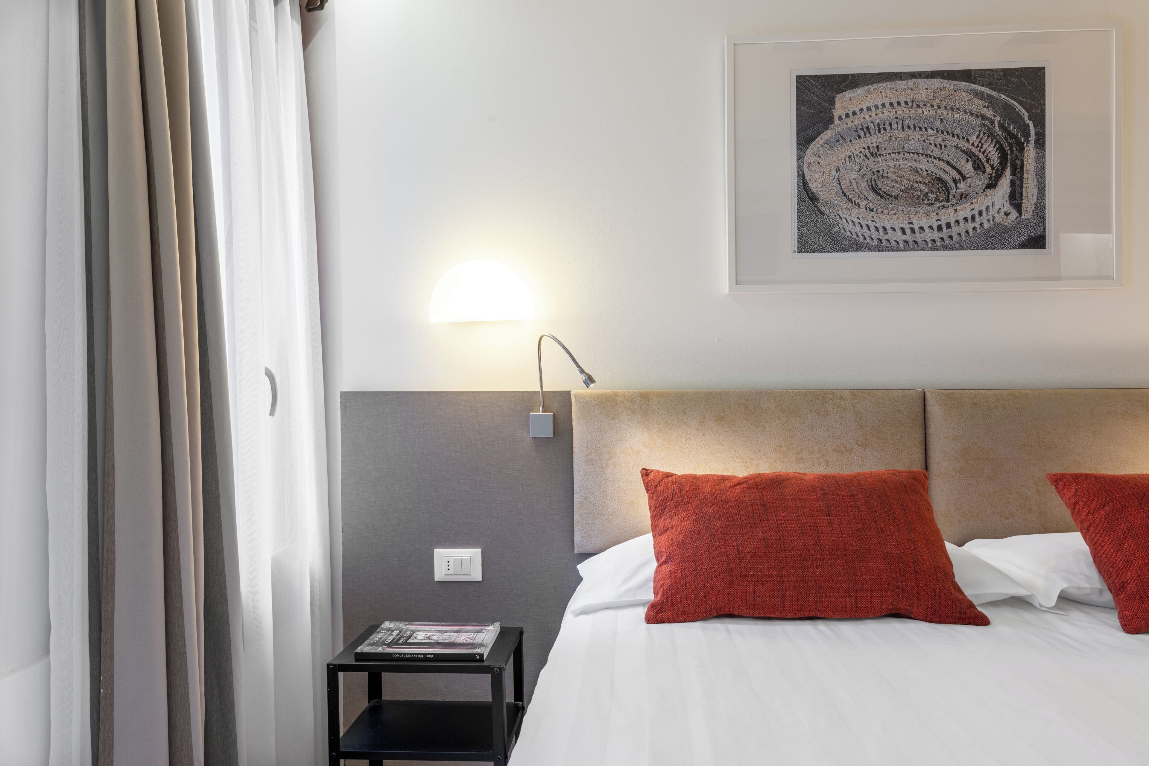 Habitación de hotel con cama, mesita de noche, lámpara, un cuadro en la pared y una ventana con cortinas.