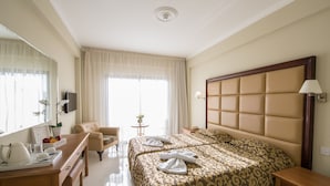 A hotel room with a large bed, a desk with a chair, a small table with a lamp, and a TV on the wall.