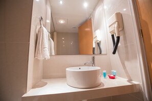 Casa de banho moderna com lavatório branco, espelho e suporte para toalhas.