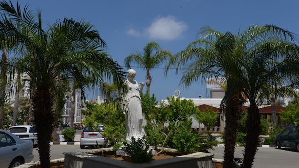 A statue in a landscaped area with palm trees and a clear blue sky.