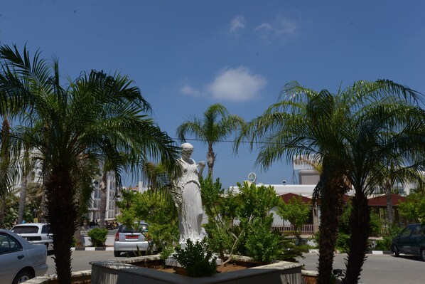 Uma estátua em área ajardinada, com palmeiras e céu azul límpido.