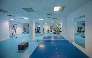 Uma academia com equipamentos de exercícios, piso azul e espelhos nas paredes.