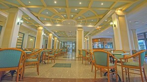 A hotel lobby with a high ceiling, chandeliers, and rows of wicker chairs. - Tsokkos Gardens (Paralimni)