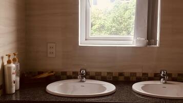 Um banheiro com duas pias, uma janela e produtos de higiene no balcão.