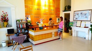 A hotel reception area with a wooden reception desk, a bookshelf, a small table with a checkered tablecloth, and a map on the wall. - Nam Long Plus Hotel (Dong Hoi)