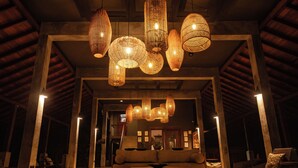 A spacious lobby with a high ceiling, multiple hanging wicker chandeliers, a central seating area with a sofa and coffee table, and a wooden floor. - Wild Grass Nature Resort (Dambulla)