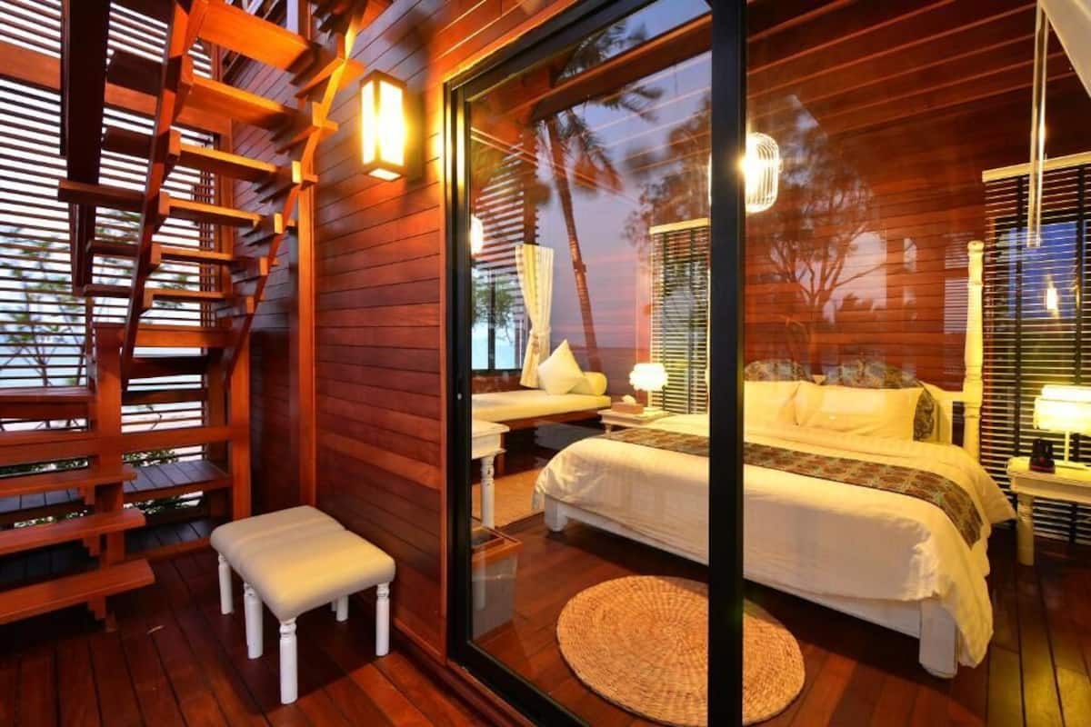 Un dormitorio con una cama grande, un pequeño banco y una escalera de madera.