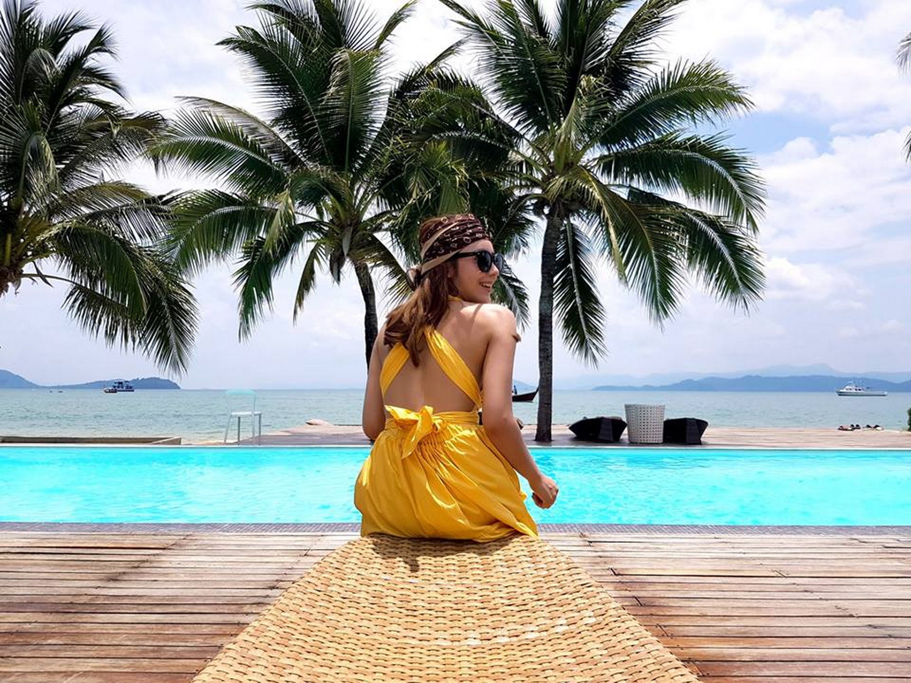 A person sitting by a pool with palm trees and a view of the sea.