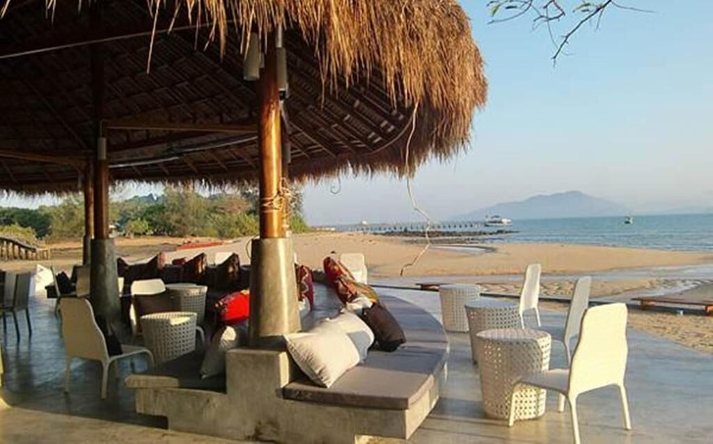 A beachside lounge with outdoor seating, a thatched roof, and a view of the sea and mountains.