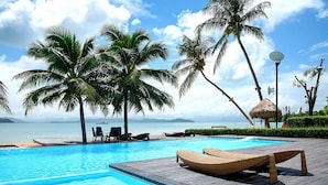 A pool area with lounge chairs, palm trees, and a view of the ocean. - The Blue Sky Resort Koh Payam (Ranong)