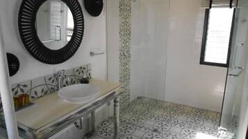 Un baño con un espejo redondo, un lavabo, una ducha y baldosas de suelo estampadas.