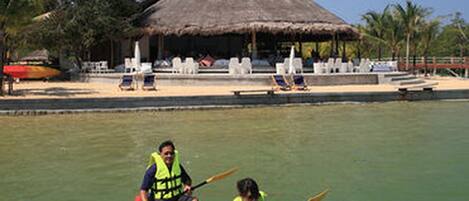A thatched-roof building with a pool and lounge chairs in the background.