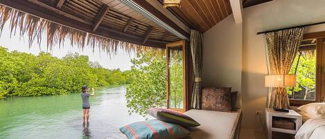 Un dormitorio con vista al río, techo de madera y mesita de noche con lámpara.