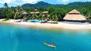 Un resort tropical con mar azul cristalino, una playa arenosa y cabañas de techo de paja.