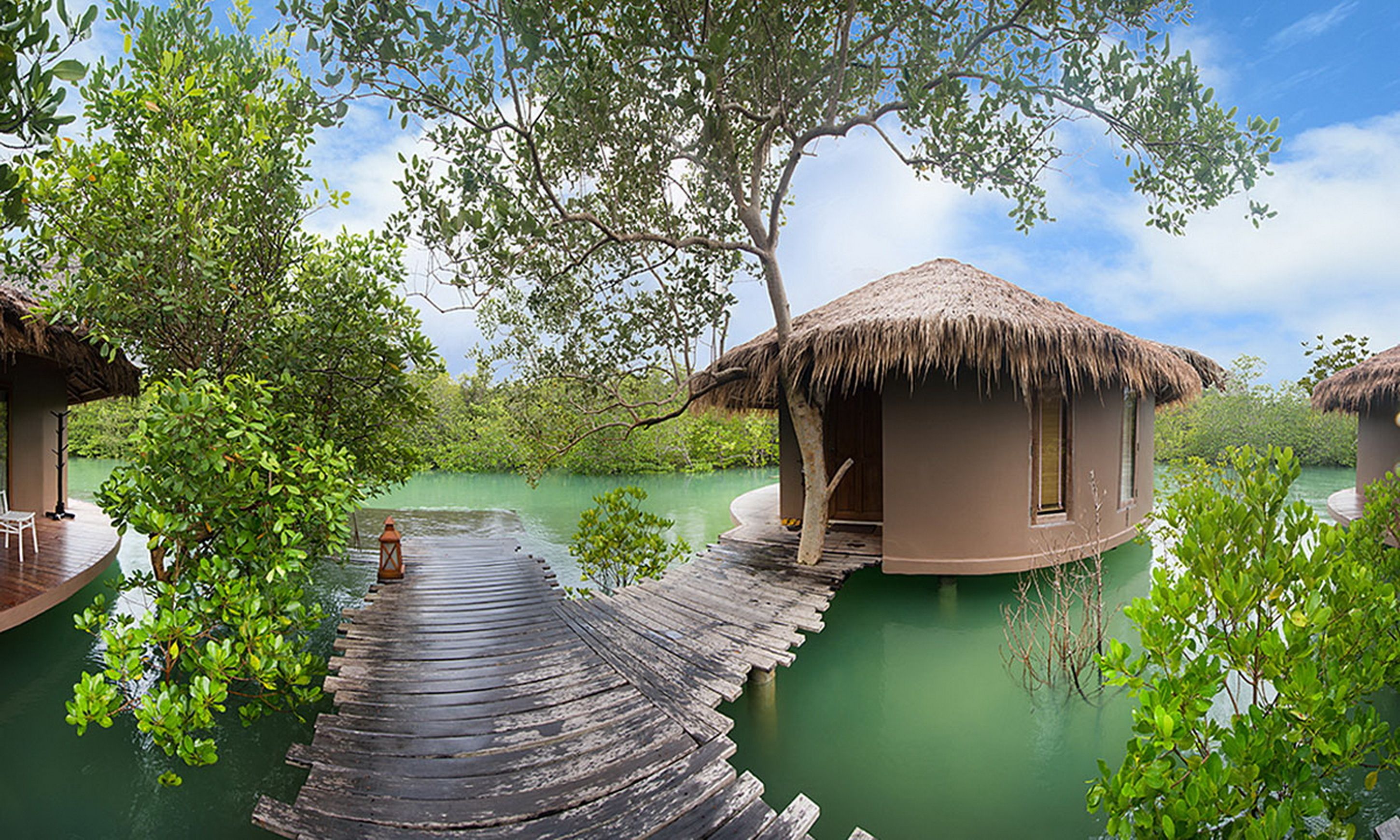 Overwater bungalows with thatched roofs connected by wooden walkways over calm water.