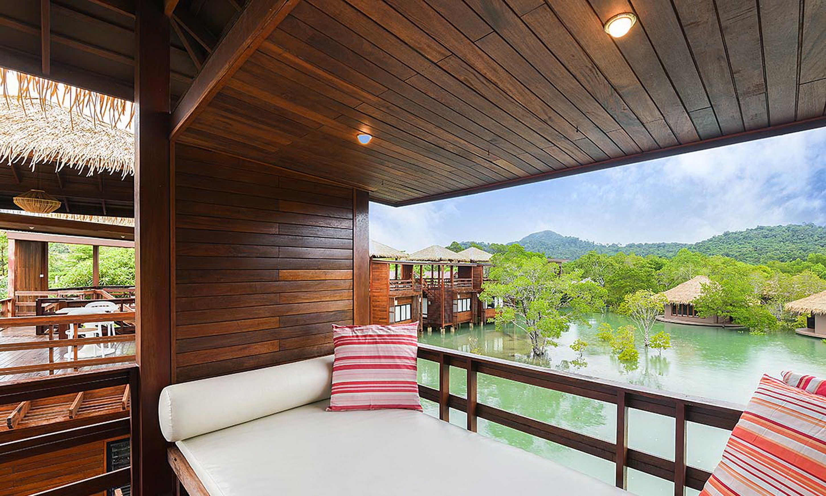 A wooden deck with a white cushioned seating area, overlooking a body of water and lush greenery.