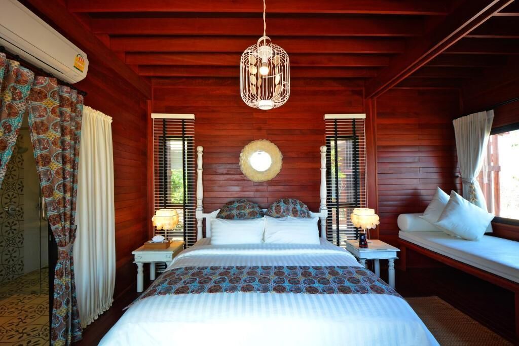 A wooden room with a bed, two nightstands, a hanging light fixture, and a window with shutters.