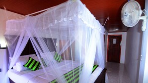 A bed with a canopy, a bedside fan, and a door in the background. - Rawana Holiday Resort (Ella)