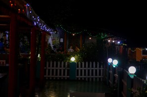 A nighttime outdoor area with string lights, a white picket fence, and a green post.