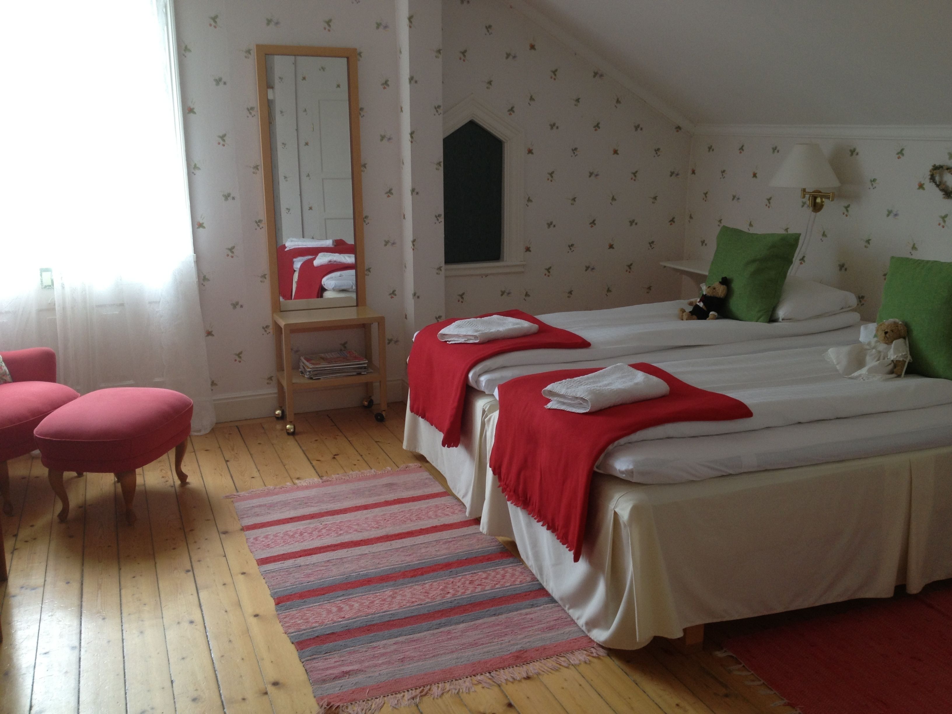 A bedroom with two beds, a mirror, a small shelf, and a window with curtains.