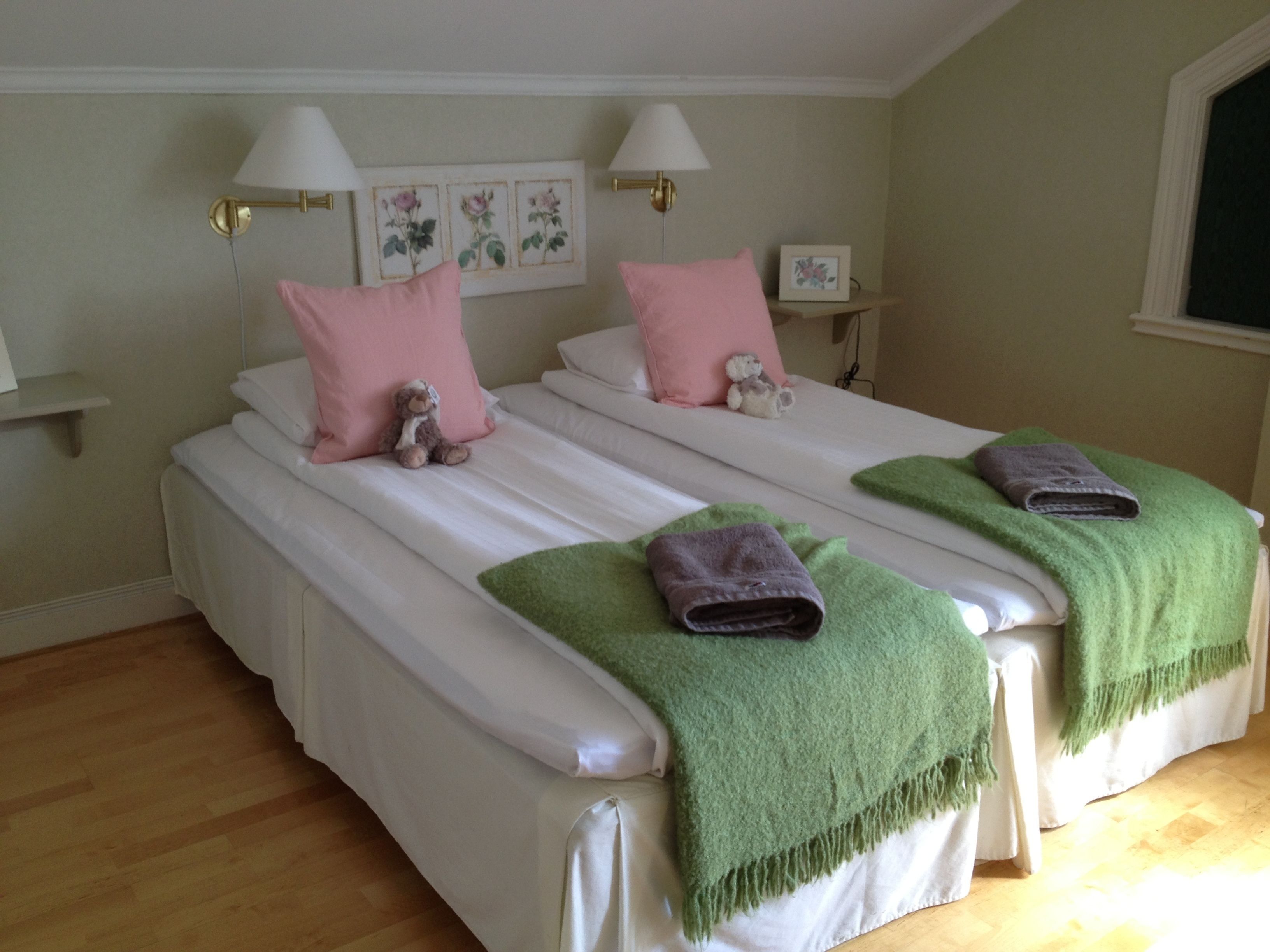 A double bed with white linens, pink pillows, and a teddy bear. There are two bedside tables with lamps and a framed picture on the wall.