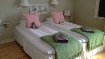 A double bed with white linens, pink pillows, and a teddy bear. There are two bedside tables with lamps and a framed picture on the wall.