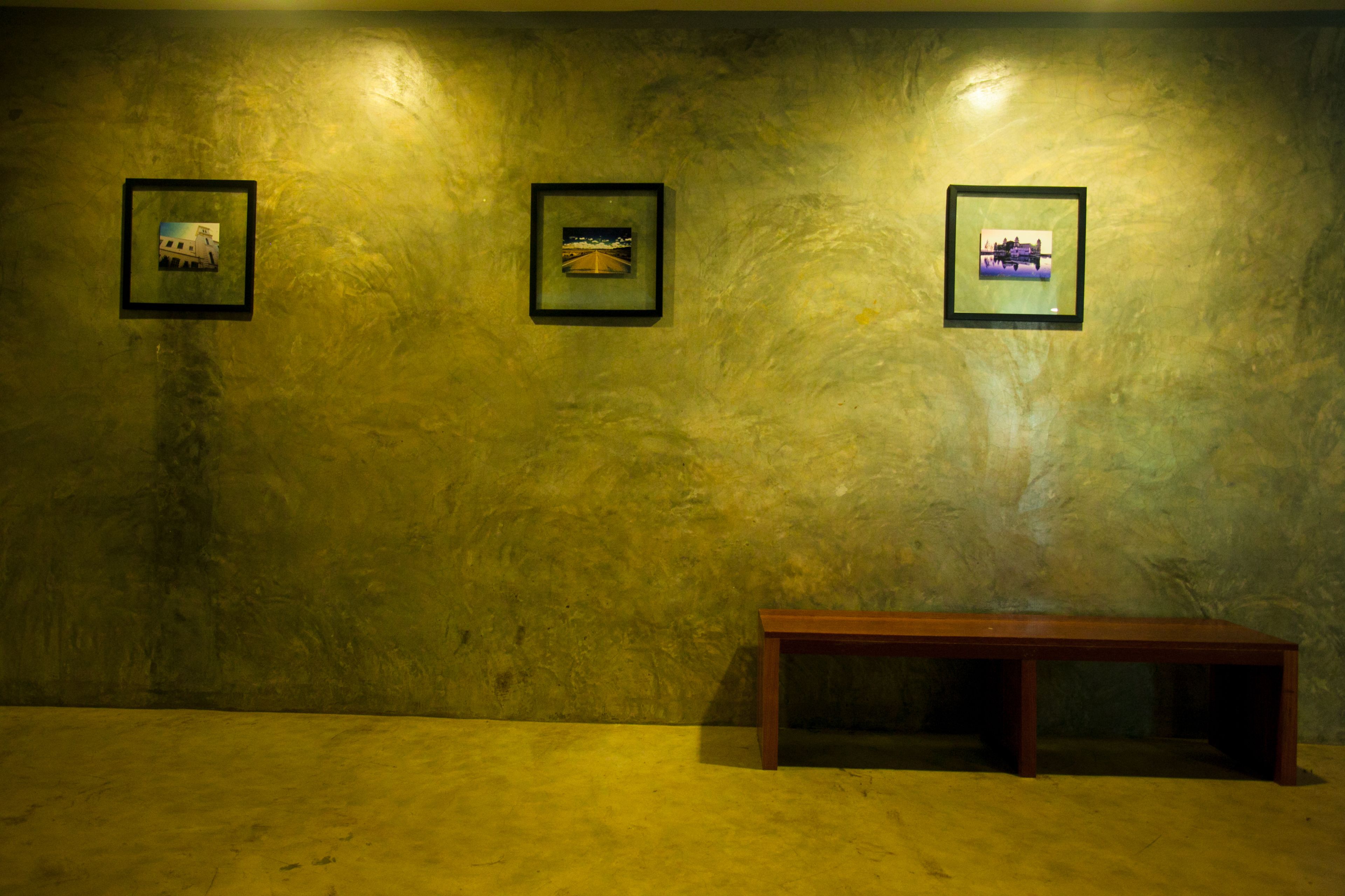 A room with a textured wall, a wooden bench, and three framed pictures.