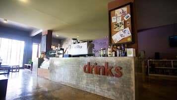 Um balcão com opções de bebidas, uma máquina de café, um mural com anotações e uma estante de livros ao fundo.