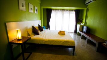 Una habitación con cama, mesita de noche, lámpara y televisor sobre una banca.
