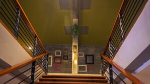 Una escalera de madera de varios niveles con barandas de metal que conduce a una plataforma con cuadros enmarcados y una planta pequeña.