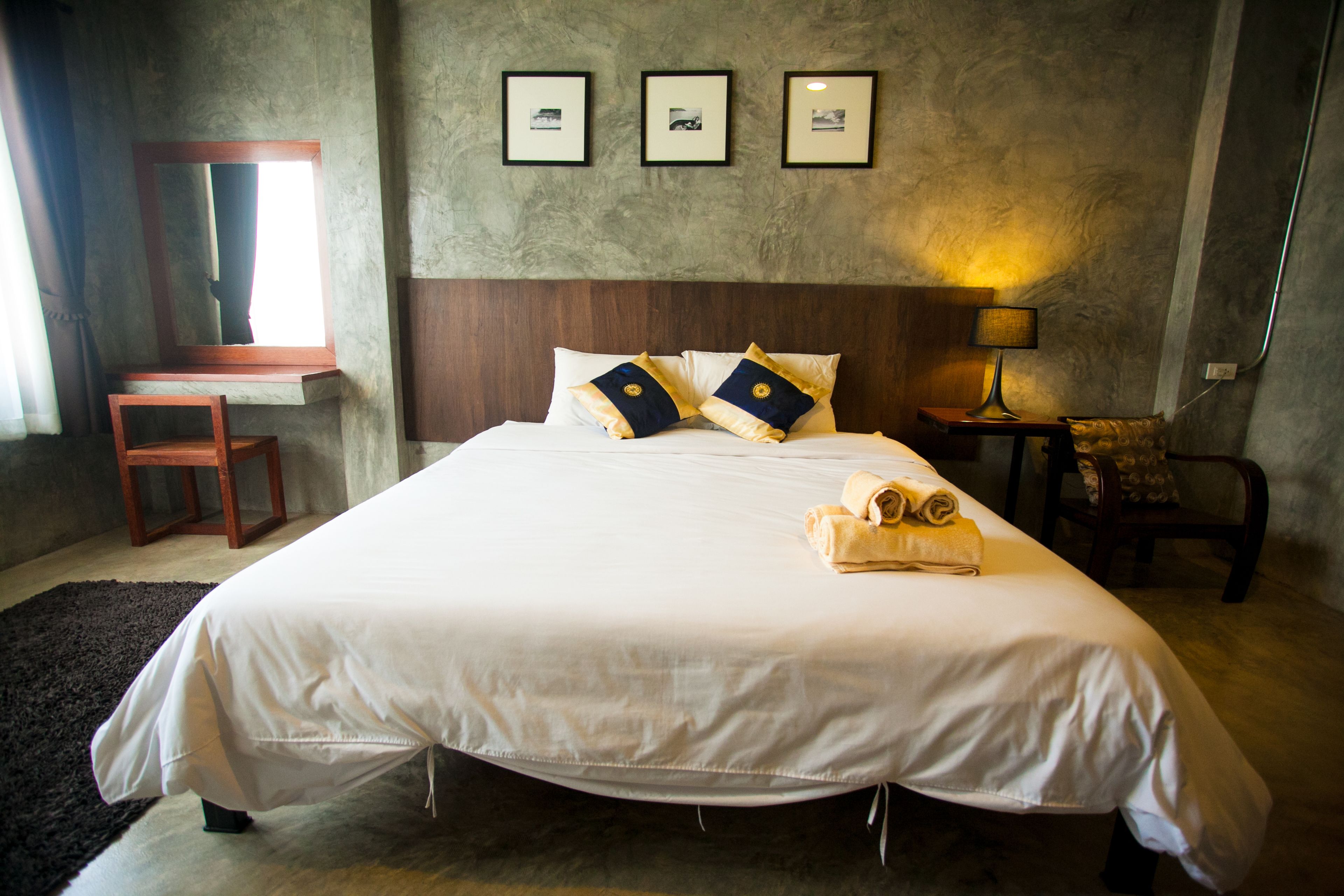 A neatly made bed with pillows, a bedside table with a lamp, a chair, and framed pictures on the wall.