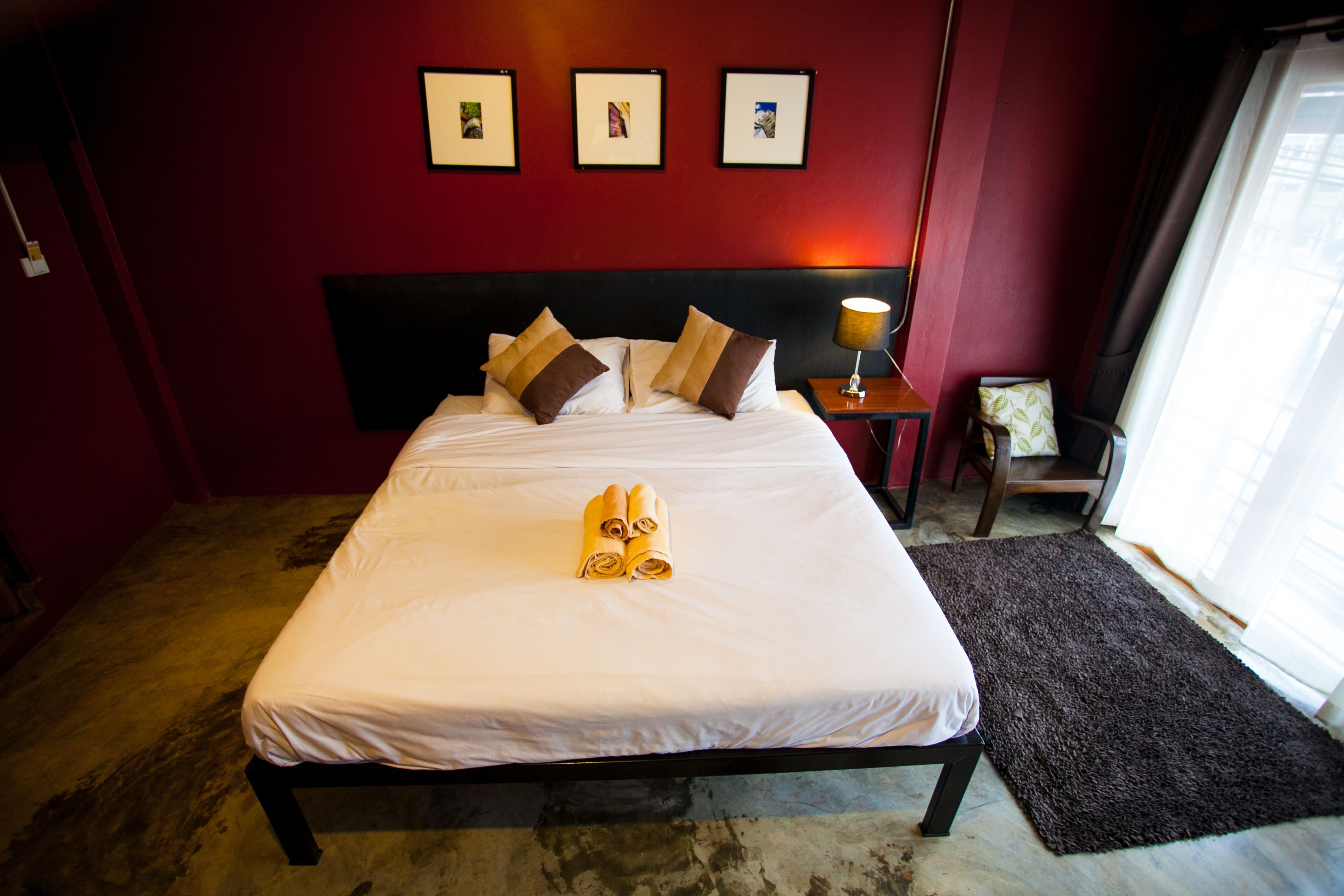 Una cama bien hecha con sábanas blancas y almohadas marrones, una lámpara de noche y tres cuadros en la pared.