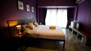 A bedroom with a bed, bedside lamp, air conditioning unit, and a television on a bench.