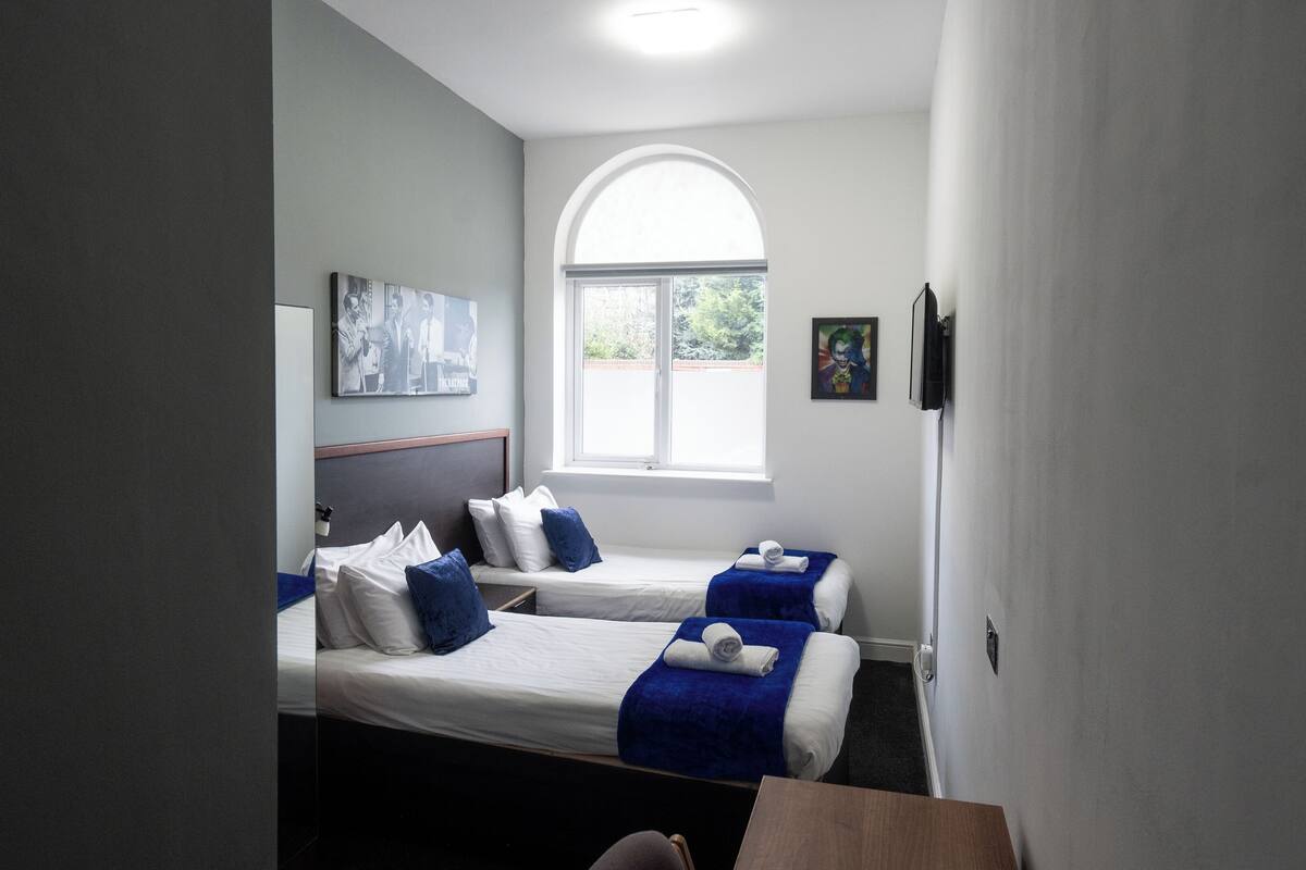 A hotel room with two single beds, a large arched window, and a painting on the wall.