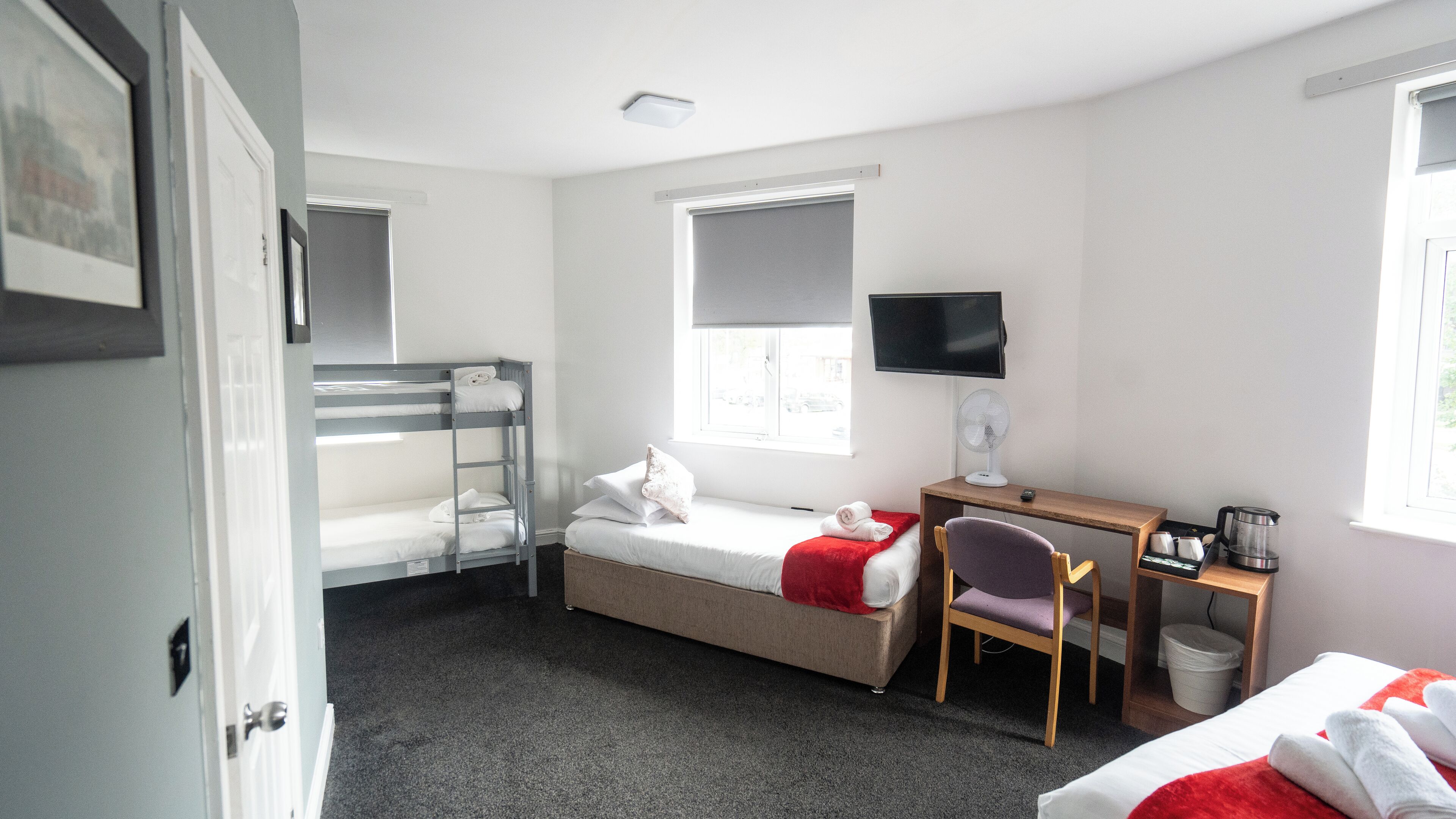 A room with bunk beds, a desk with a chair, a television, and a window.