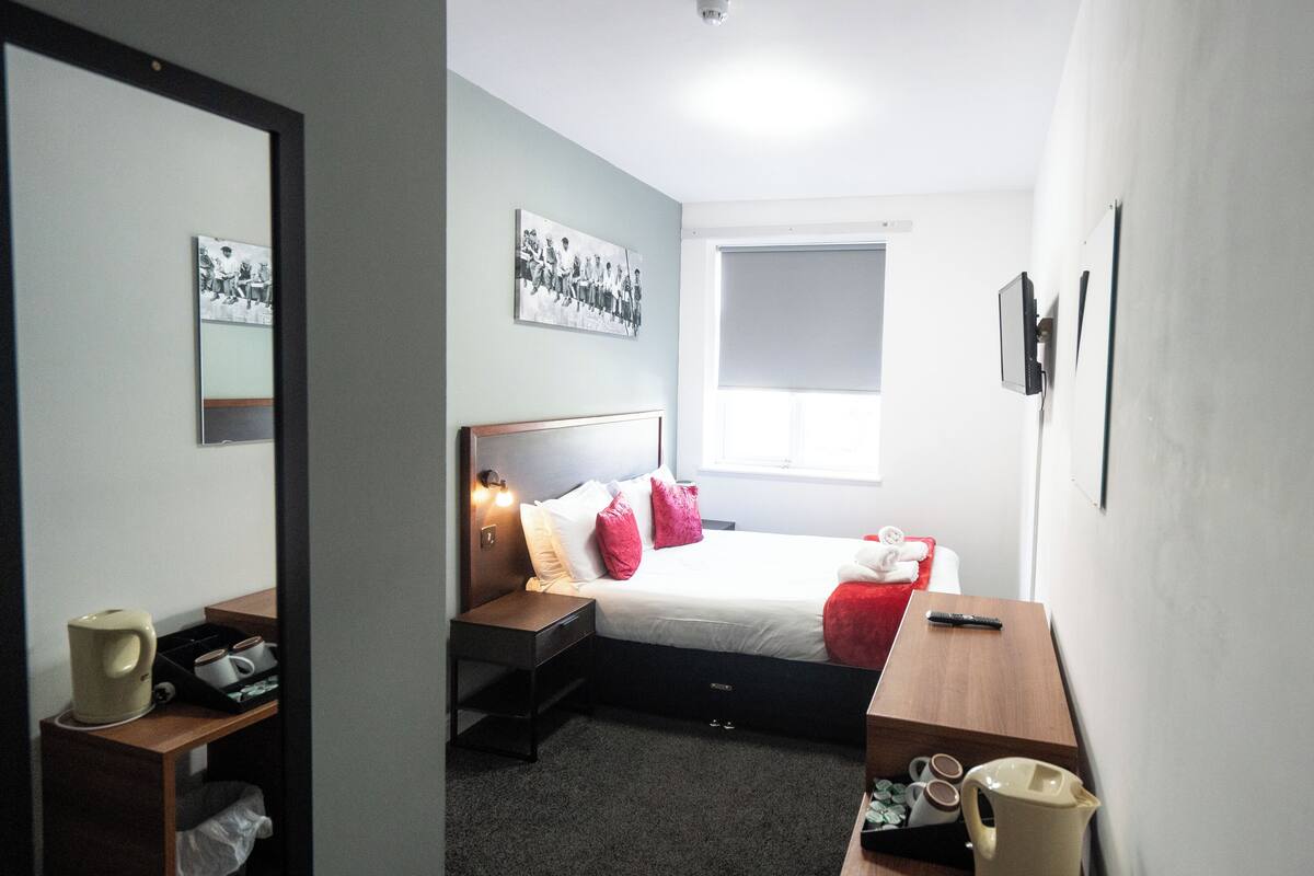 A hotel room with a bed, bedside tables, a desk, a chair, a window, and a mirror.