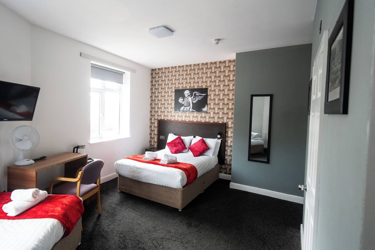 A hotel room with two beds, a desk, a chair, a TV, and a window.