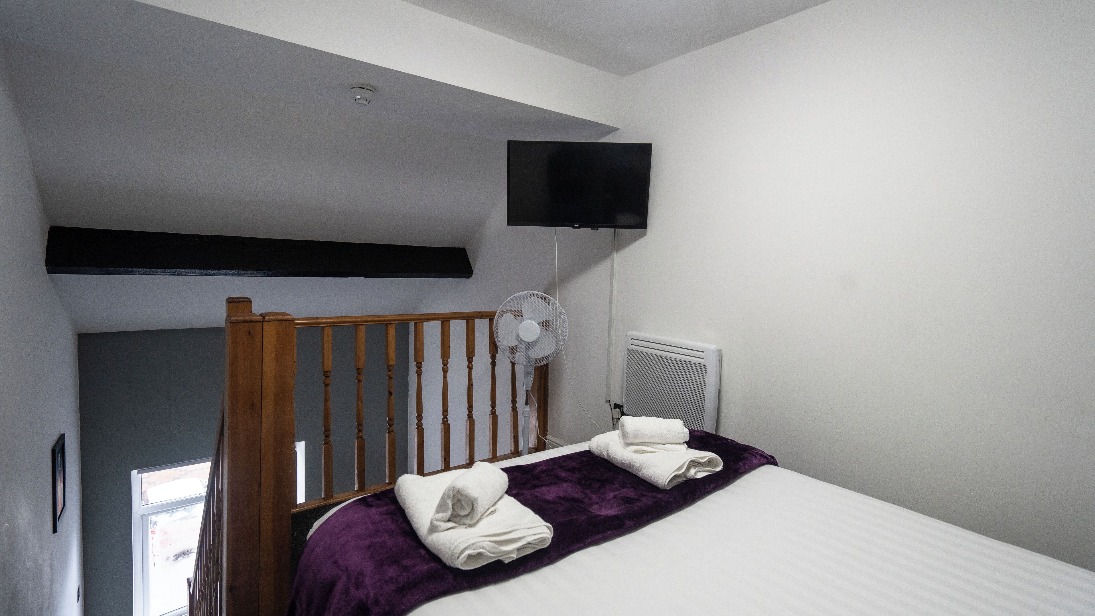 A bedroom with a bed, a fan, a mounted TV, and a window.