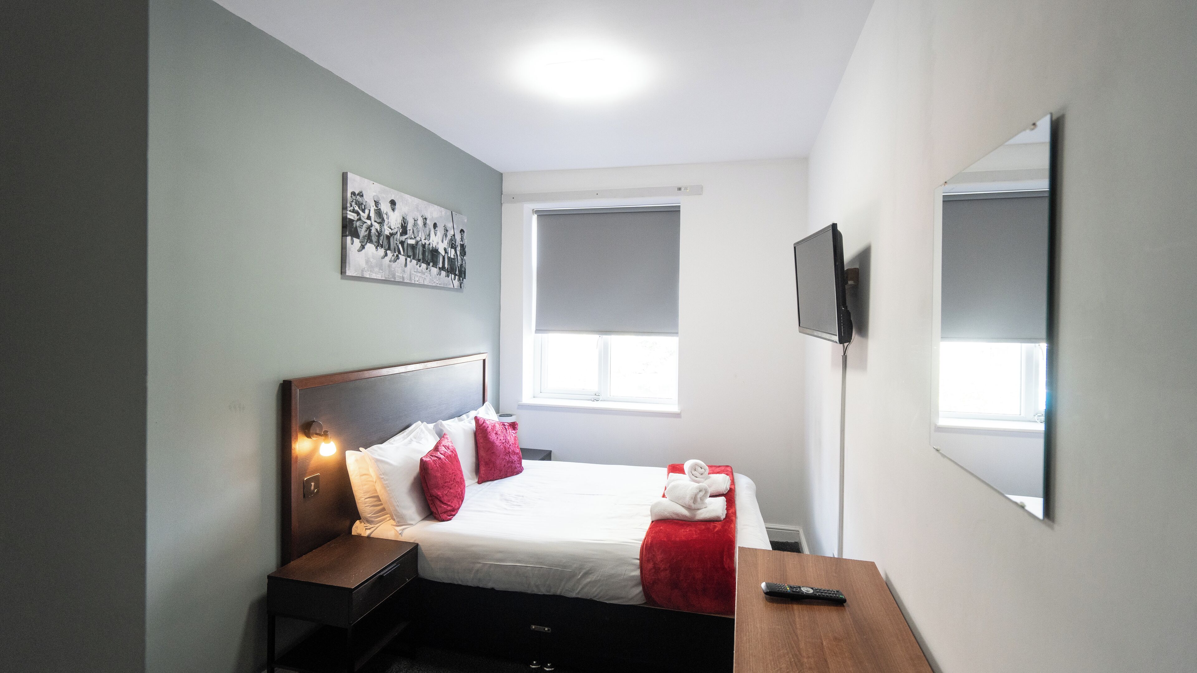 Ein Schlafzimmer mit einem Bett, einem Nachttisch und einem an der Wand befestigten Fernseher.