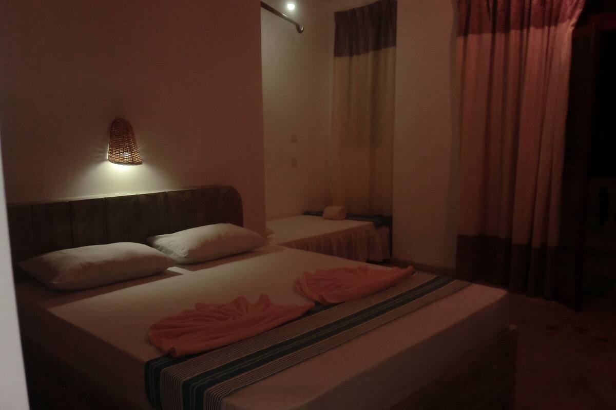 A hotel room with a bed, two pillows, a bedside table, a lamp, and a window with curtains.