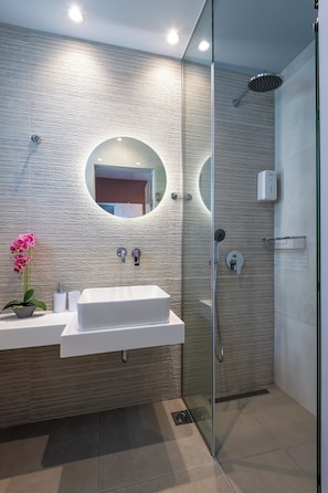 A modern bathroom with a glass-enclosed shower, a round mirror, and a white sink.