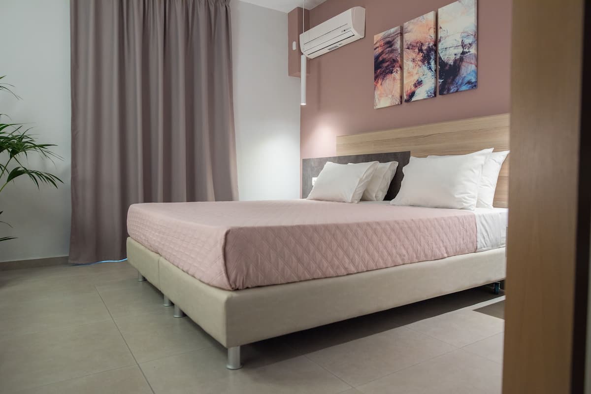Ein modernes Schlafzimmer mit einem großen Bett, einer Kopfteil, einer Klimaanlage und abstrakter Wandkunst.