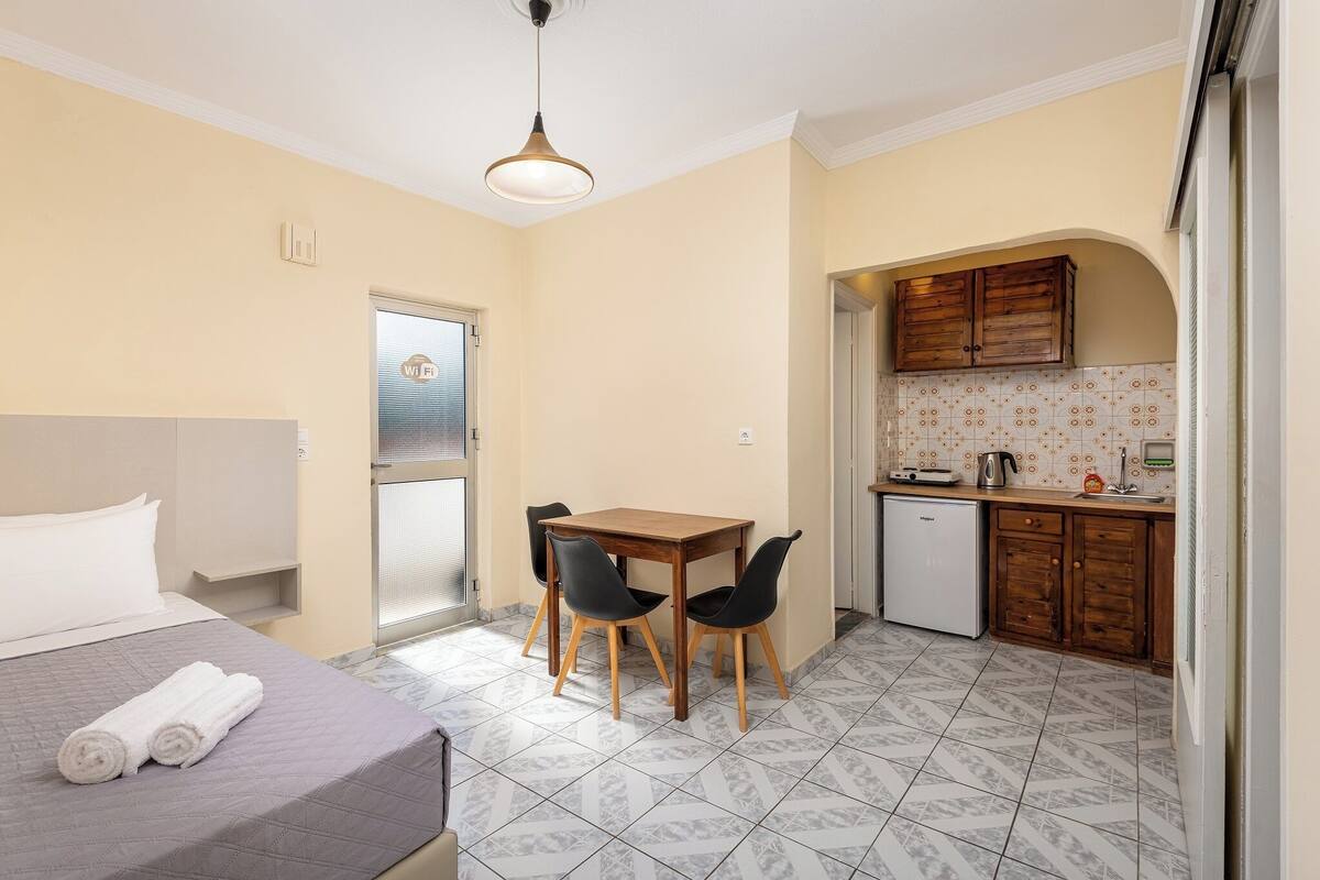 Ein Hotelzimmer mit Bett, Tisch mit Stühlen, einer Küchenzeile und einer Tür zu einem Balkon.
