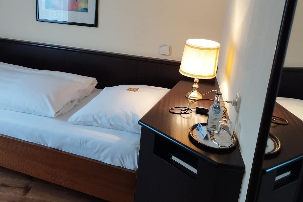 Un lit bien fait, avec du linge de lit blanc, une table de chevet avec une lampe et un tableau encadré au mur.