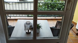 Une vue à travers une fenêtre donnant sur un coin repas, avec une table et des chaises, une plante en pot et une lanterne en métal.