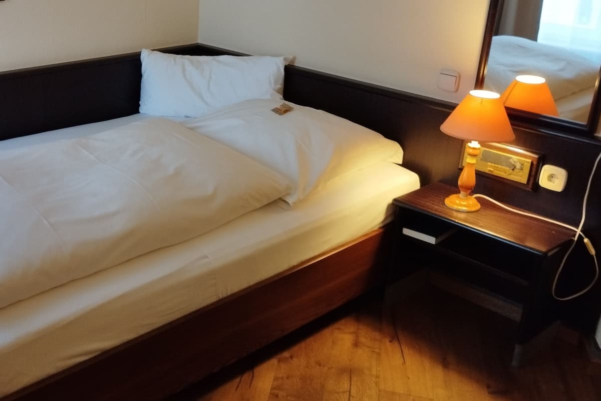 Un lit bien fait, avec du linge de lit blanc, une table de chevet avec une lampe et un miroir qui reflète le lit.